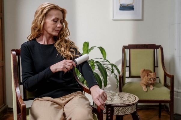A Caucasian Woman Removing Lint off the Top She’s WearingWhile a Cat Sits Nearby