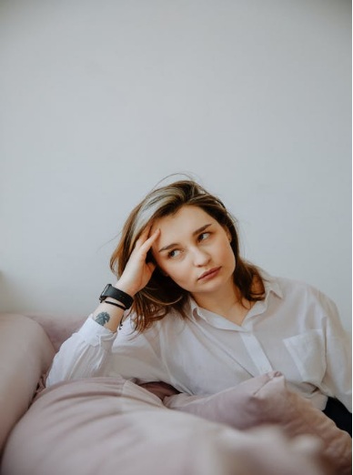 A Caucasian Woman Sitting on a Couch, and Looking off to the Side with a Contemplative Look on Her Face