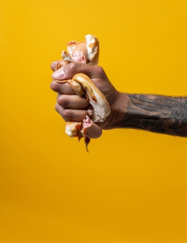 A Handhaving a Tattooed Forearm Squishing a Hotdog in its Fist