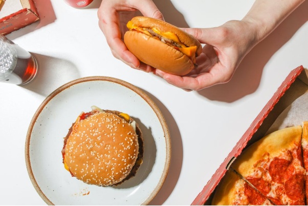 A Hand Holding a Cheeseburger with a Separate Burger, Pie, and Drink in Front of them