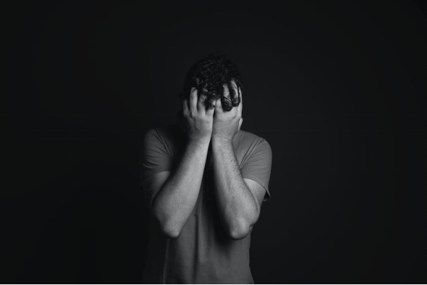 An Achromatic image of a Man Wearing a T-Shirt Covering His Face with Both Hands