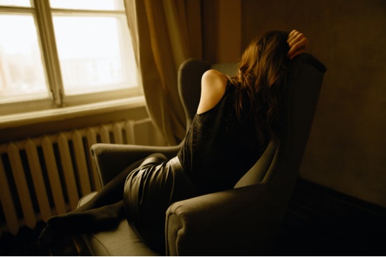 A woman hides her face while sitting in a chair in an empty room