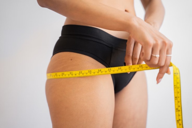 A-woman-measures-her-hips-with-a-measuring-tape-indicating-weight-loss.