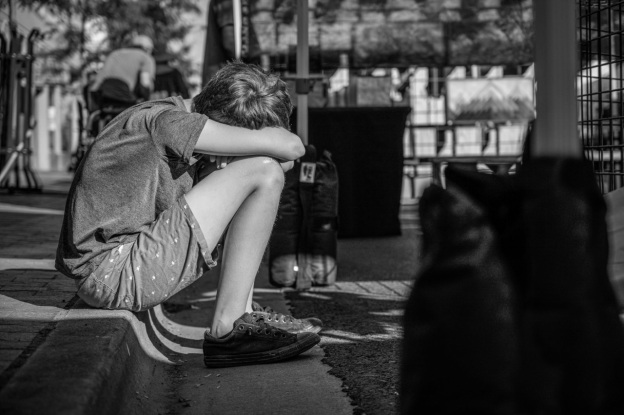 A black and white photo of a young boy looking depressed as he hides away