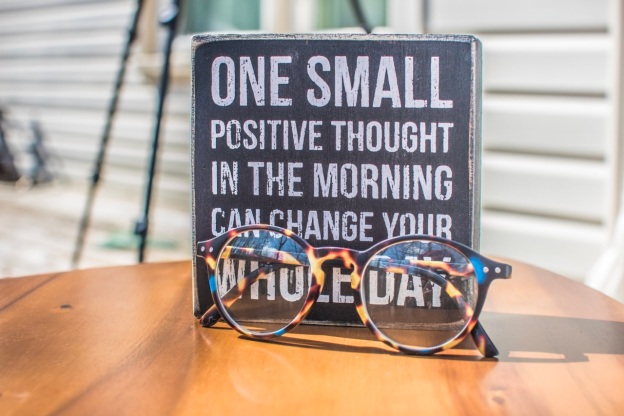 A daily affirmation board and a pair of glasses are placed on a table