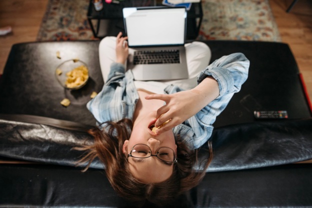 A depressed young girl binges on chips while on her laptop