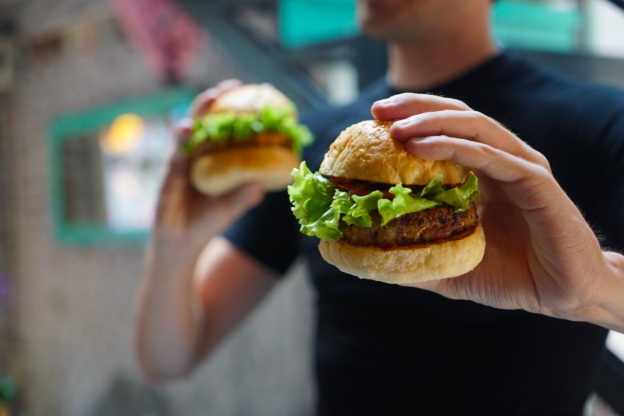 A person holds a burger in each hand, ready to eat them