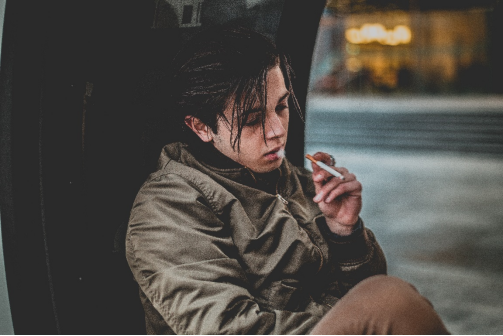 A person wearing a green jacket, smoking a cigarette