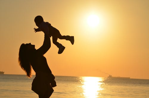 a mother holding her child in the air near the sea