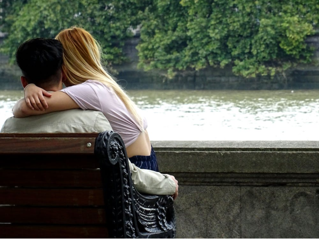 A man and a woman sitting together on a bench facing a river